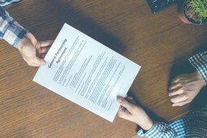 two business partners sign partnership agreement in the office table overhead toned image